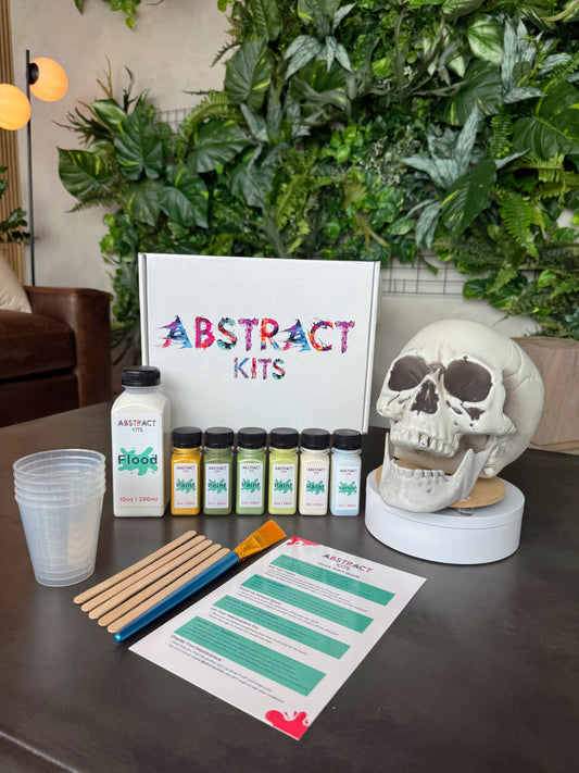 Skully fluid art kit by Abstract Kits, featuring a blank 8-inch acrylic skull sculpture alongside paint, flood, varnish, mixing cups, guide, and all included DIY art supplies.