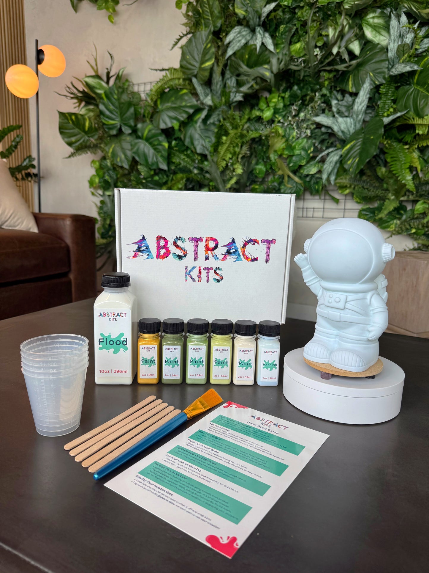 Interstellar fluid art kit by Abstract Kits, featuring a blank 8-inch acrylic astronaut sculpture alongside paint, flood, varnish, mixing cups, guide, and all included DIY art supplies.